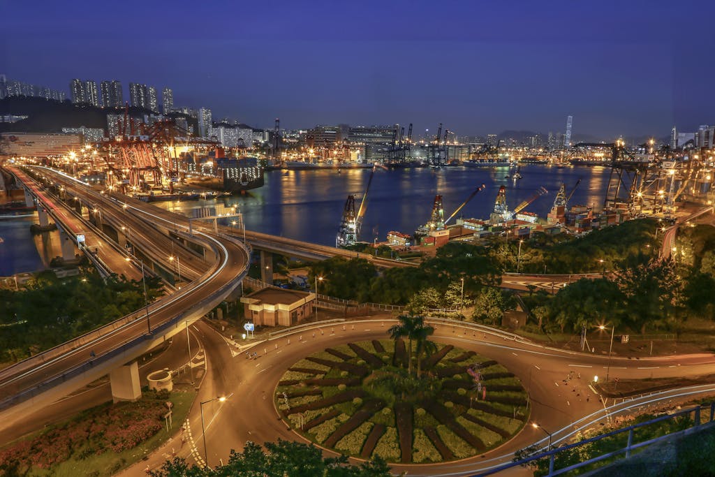 A breathtaking nighttime view of a bustling harbor with illuminated roads and city lights reflected on the water.
